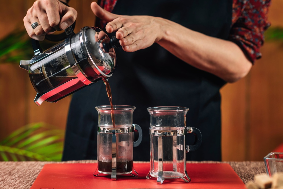 French Press Coffee. Hands of female barista pouring French press coffee in glass coffee mug