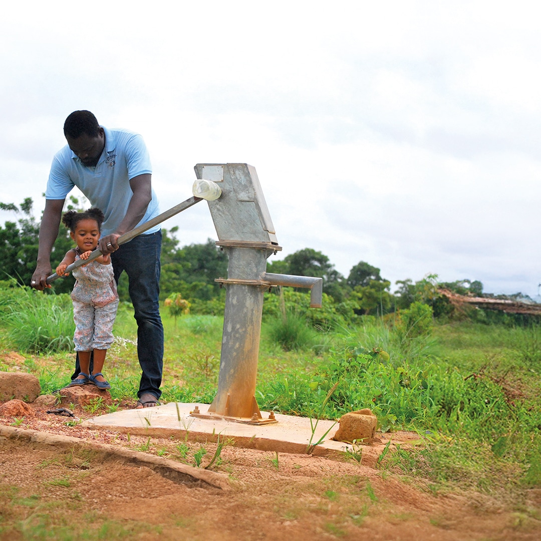father helping child pump water in africa