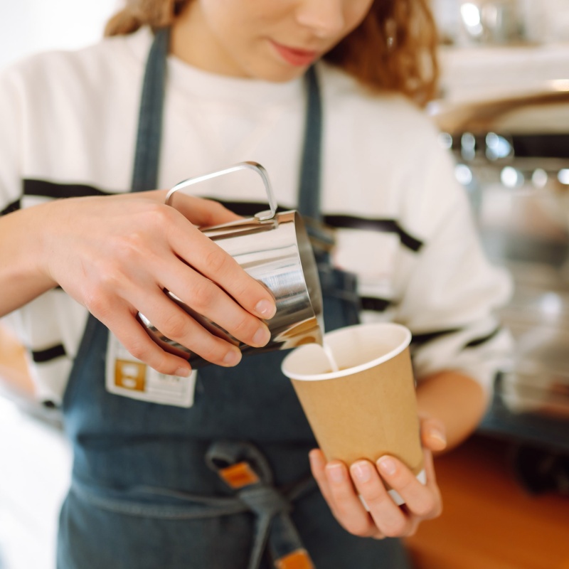 Coffee barista pouring milk in to takeaway cup
