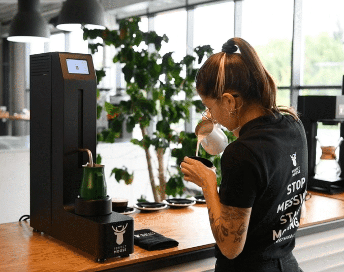 Barista creating latte art next to a Perfect Moose Jack Milk Steamer