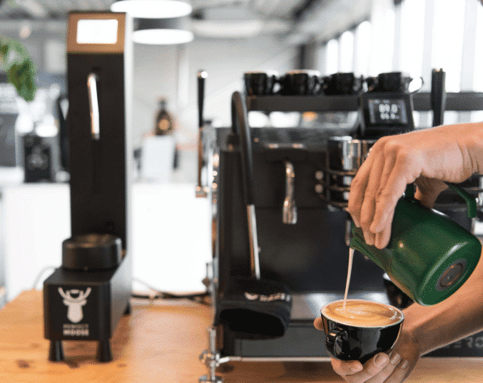 Barista creating latte art next to a Perfect Moose Jack Milk Steamer