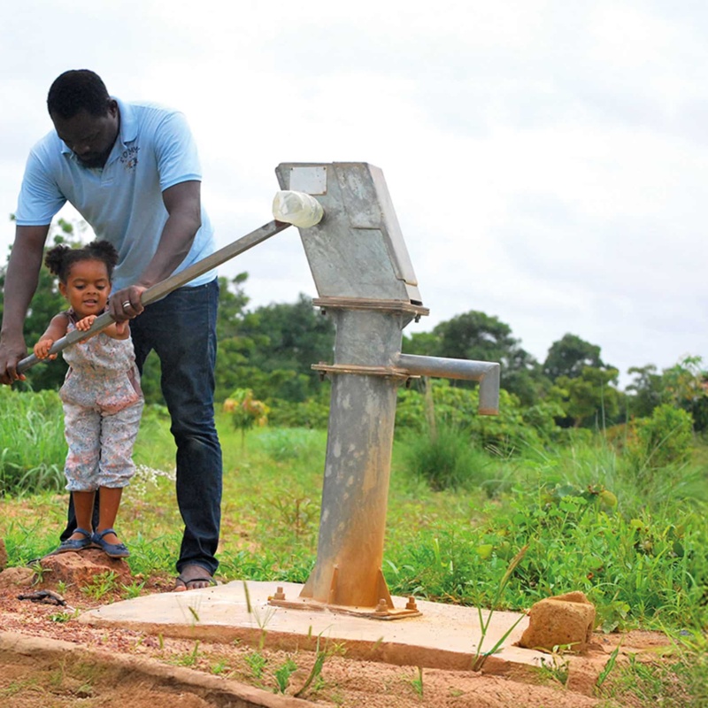 father helping child pump water in africa