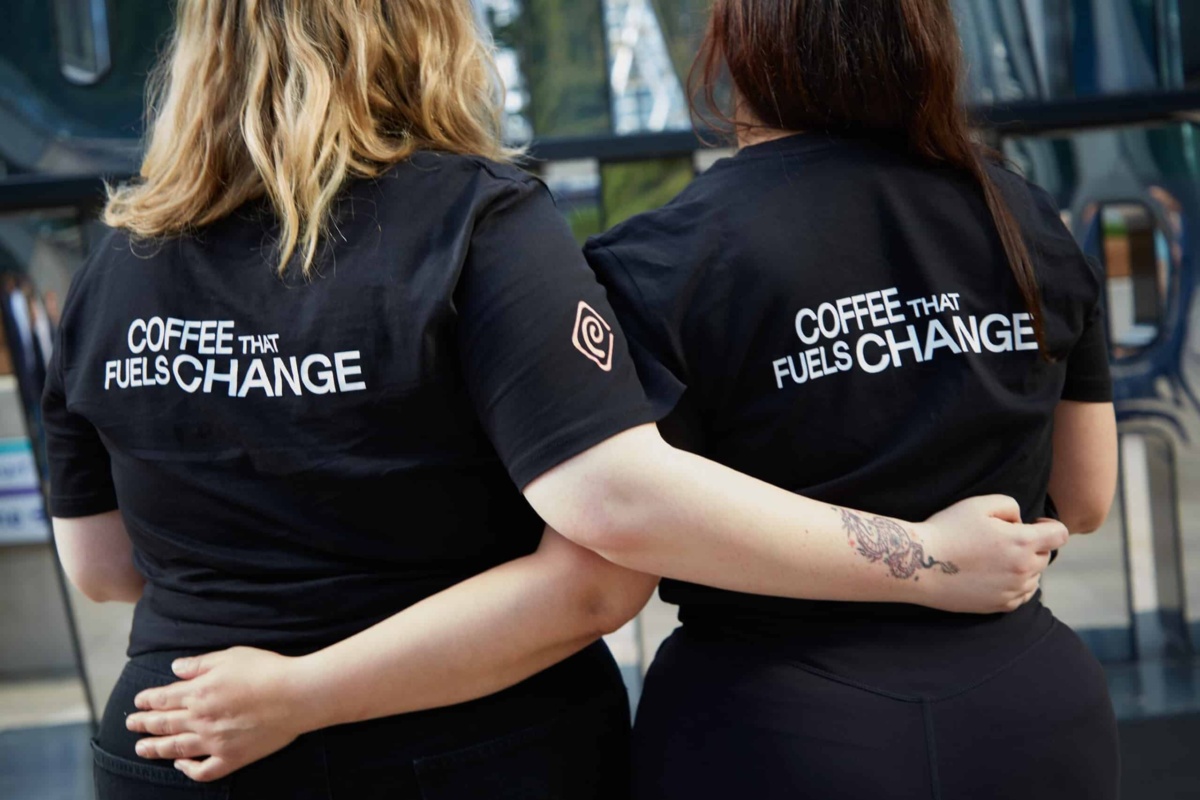 Two women wearing Coffee that Fuels Change t-shirts