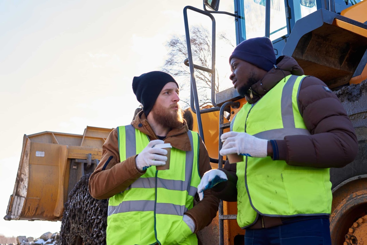Two trade workers with coffee in paper cups by digger