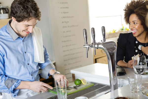 Chrome triple-faucet drinks tap installed on a countertop with an integrated drip tray, alongside glasses and fresh citrus in a hospitality environment.