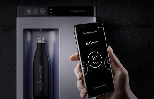Hand holding smartphone that is displaying the Borg and Overstrom app. In the background a countertop water dispenser is filling a sports bottle