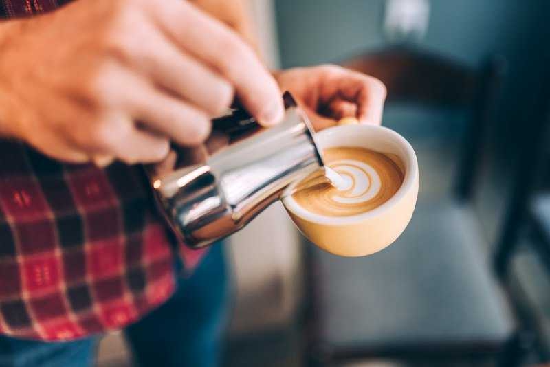 barista pouring milk into coffee