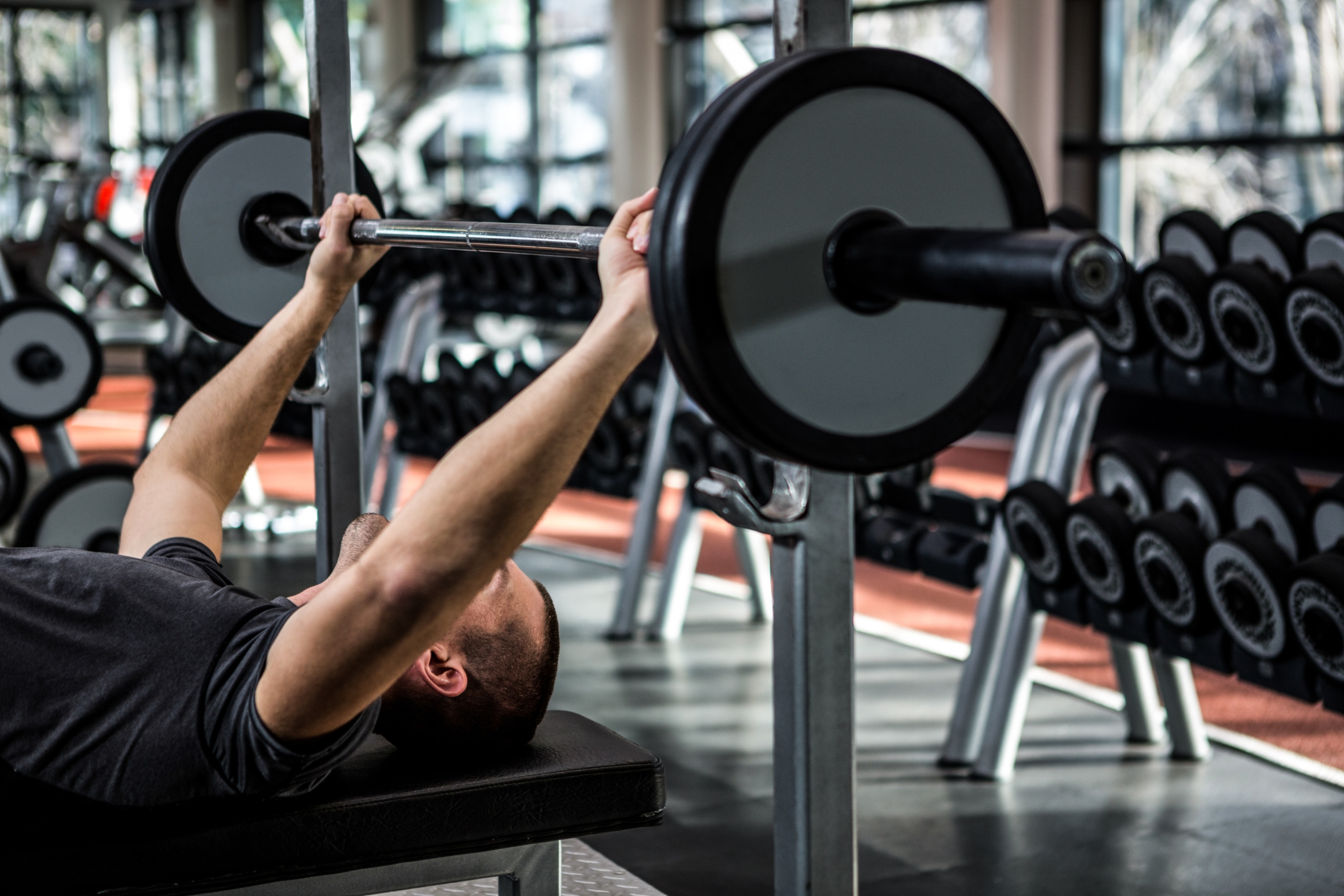 Muscular man lifting barebell while lying on bench at gym