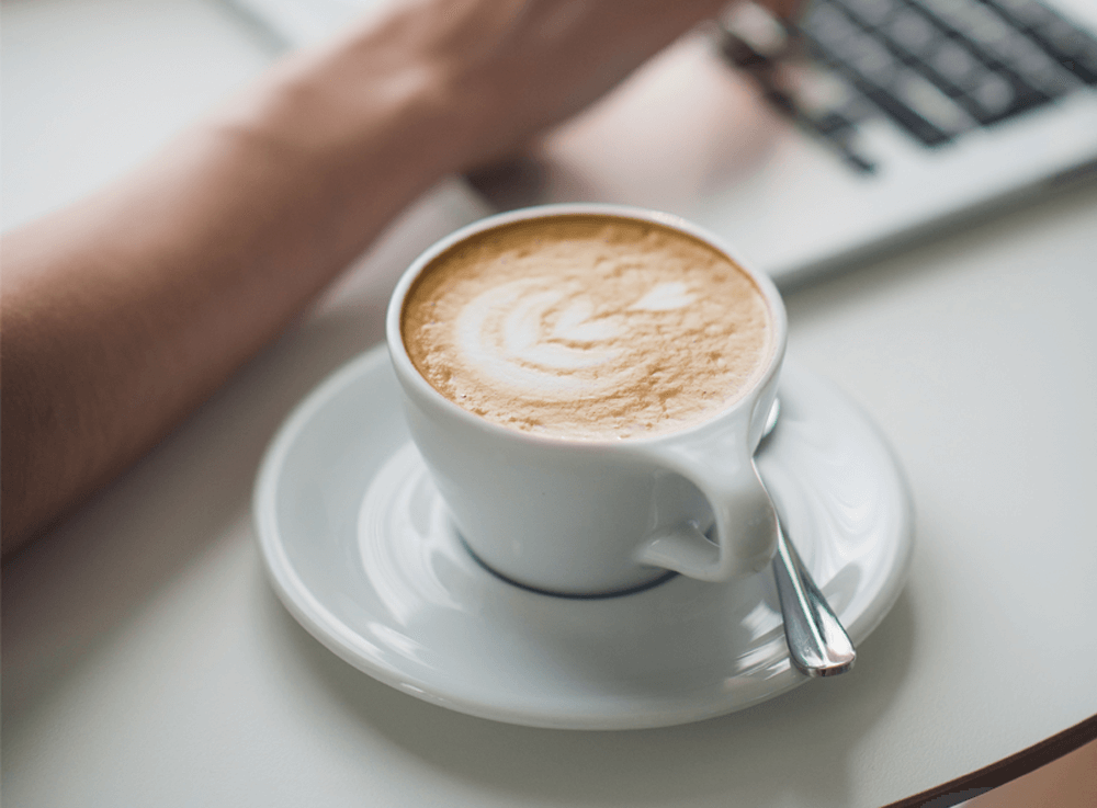 Cup of coffee next to a person working on a laptop