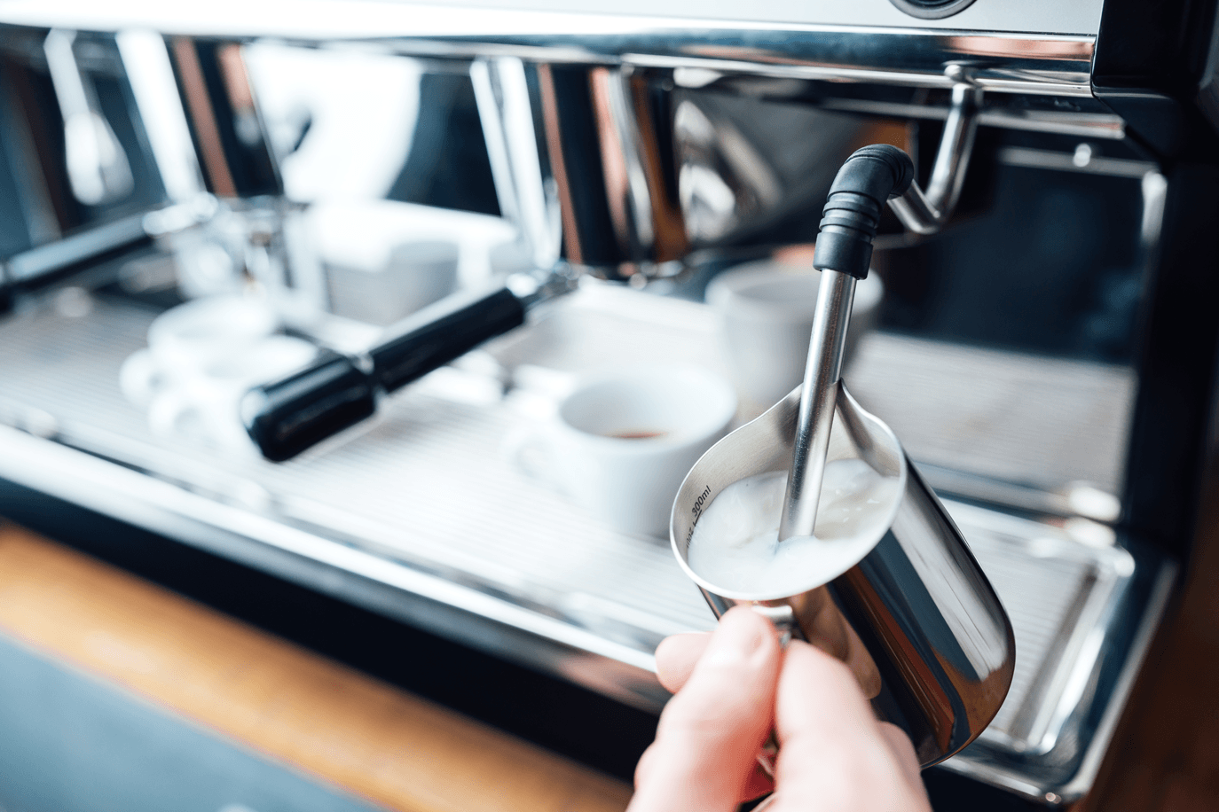 Barista using a steam want to froth milk in a jug